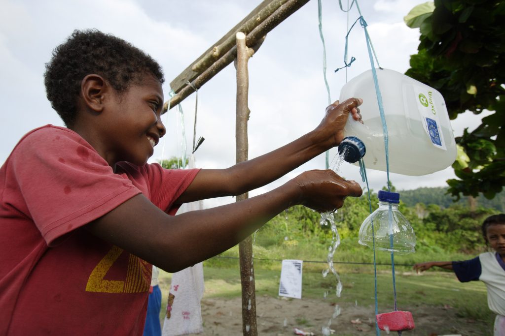 Dani, 11, uses a Tippy Tap after a hygiene game at the the community event at SDN Waharia elementary school. Sanitation kit bags containing games, activities and information were used to promote hygiene practices and hand washing. Primari (Partner) and Oxfam staff assisted trained cadres to run the outdoor games.Nabire, Papua, Indonesia. Indonesia is one of the most natural disaster-prone countries in the world. It is located at the friction points of three continental tectonic plates and is prone to seismic activities such as earthquakes and tsunamis. A significant proportion of the populations affected by small or medium scale disasters are deprived from their right to life and dignity. Disaster events push socio-economically marginalized people into poverty, increasing their dependency on natural resources. This, in turn, degrades the environment and further increases their vulnerability to disaster risk. Despite the growing understanding and acceptance of the importance of disaster risk reduction and increased disaster response capacities, disasters and the management and reduction of risk continue to pose a challenge.Casual observation indicates that over the past decade there has been an increased frequency in natural disasters.  The plight of chronically vulnerable communities. Recurring disasters also pose a great development challenge for all countries in Asia, and particularly in Indonesia. In several provinces, poor and chronically disaster-prone communities continue, year after year, to be vulnerable to recurrent disasters such as flood, drought and forest fire.